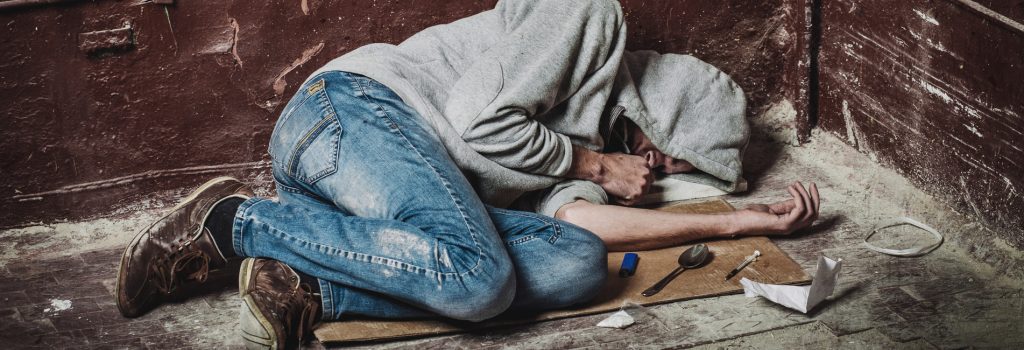 Heroin Addiction Treatment in Sun City Emerald Isle - A man lays passed out after shooting heroin on a cardboard box in an alley. He needs Heroin Addiction Treatment in Sun City to get better.