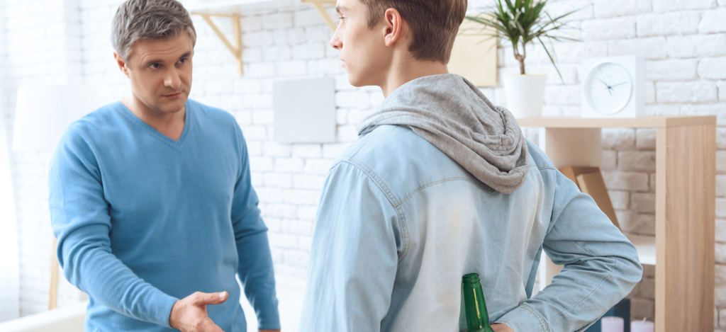 Signs of Addiction Emerald Isle Health and Recovery - A father is confronting his son who is hiding a beer bottle behind his back about his signs of addiction.