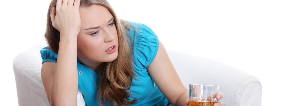 Alcohol Rehab - A woman sits with her hand on her head and a drink on the other. Her frequent heavy drinking means she needs a residential alcohol rehab to get sober.