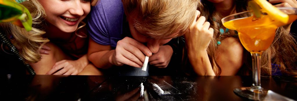 Cocaine Addiction Treatment - A man out for a night of parting has a female friend on each side of him as he does some coke. Next to hin is a drink. Cocaine addiction treatment helps those addiction to cocaine and also other drugs like alcohol.