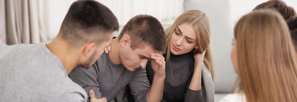 Family Therapy Mental Health - Several family members console a young man as he talks about his depression. Family therapy helps all members of the family understand and support the treatment their loved one is going through.